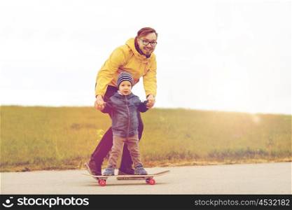 family, childhood, fatherhood, leisure and people concept - happy father teaching little son to ride on skateboard