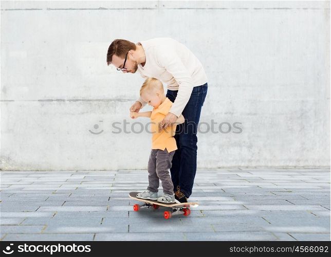 family, childhood, fatherhood, leisure and people concept - happy father teaching little son to ride on skateboard over urban street background