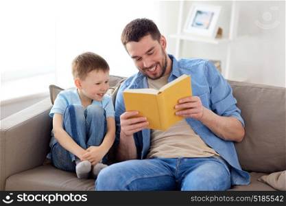 family, childhood, fatherhood, leisure and people concept - portrait of happy smiling father and little son reading book on sofa at home. happy father and son reading book sofa at home