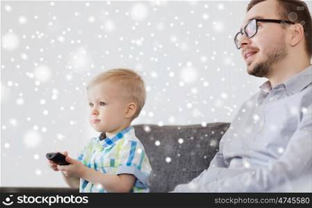 family, childhood, fatherhood, technology and people concept - happy father and little son with remote control watching tv at home over snow