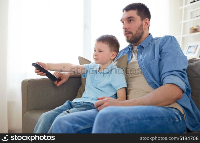 family, childhood, fatherhood, technology and people concept - happy father and little son with remote control watching tv at home. father and son with remote watching tv at home