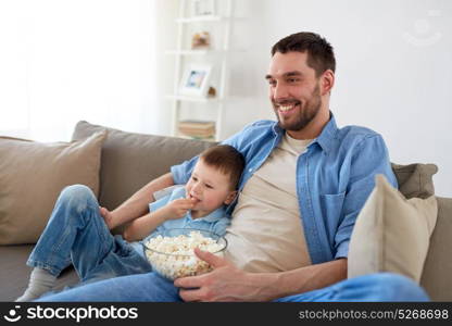 family, childhood, fatherhood, technology and people concept - happy father and little son with popcorn watching tv at home. father and son with popcorn watching tv at home