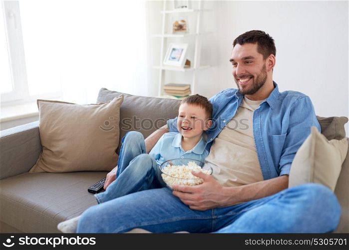 family, childhood, fatherhood, technology and people concept - happy father and little son with remote control and popcorn watching tv at home. father and son with popcorn watching tv at home