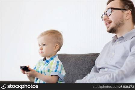 family, childhood, fatherhood, technology and people concept - happy father and little son with remote control watching tv at home