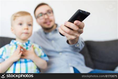 family, childhood, fatherhood, technology and people concept - happy father and little son with remote control watching tv at home