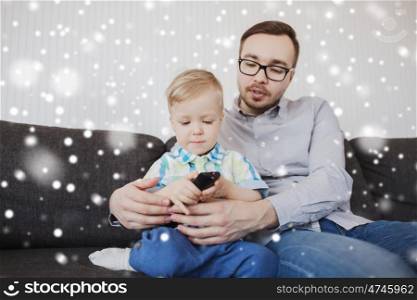 family, childhood, fatherhood, technology and people concept - happy father helping little son with remote control and watching tv at home over snow