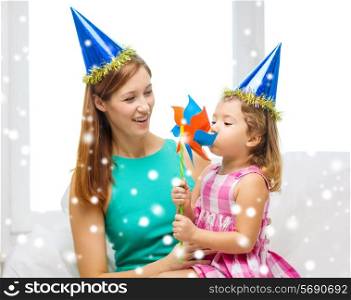 family, childhood, holidays and people concept - happy mother and daughter in blue party hats with pinwheel toy