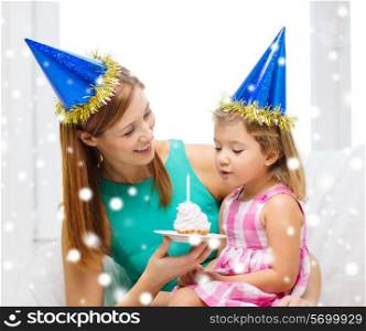 family, childhood, holidays and people concept - happy mother and daughter in blue party hats with cake and candle