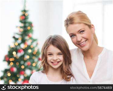 family, childhood, holidays and people - smiling mother and little girl over living room and christmas tree background