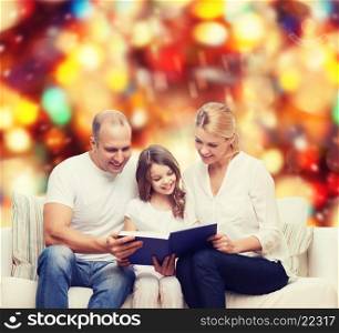 family, childhood, holidays and people - smiling mother, father and little girl reading book over red lights background
