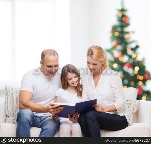 family, childhood, holidays and people - smiling mother, father and little girl reading book over living room and christmas tree background