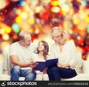 family, childhood, holidays and people - smiling mother, father and little girl reading book over red lights background