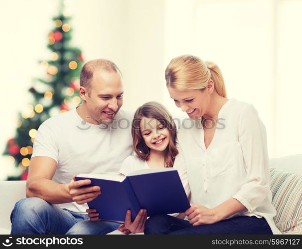 family, childhood, holidays and people - smiling mother, father and little girl reading book over living room and christmas tree background