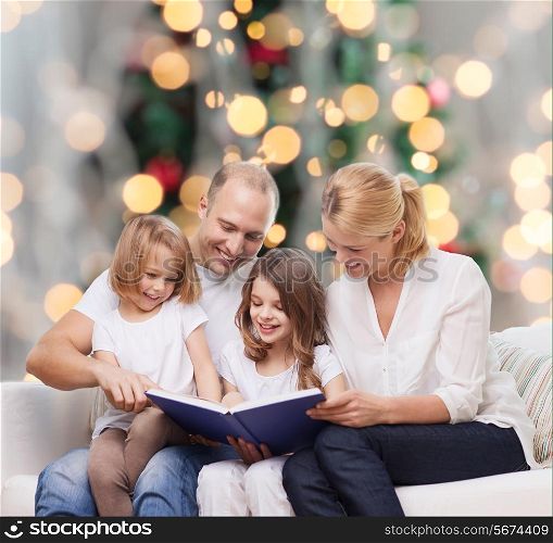 family, childhood, holidays and people - smiling mother, father and little girls reading book over living room and christmas tree lights background