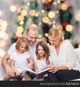 family, childhood, holidays and people - smiling mother, father and little girls reading book over living room and christmas tree background