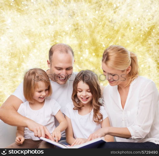 family, childhood, holidays and people - smiling mother, father and little girls reading book over yellow lights background