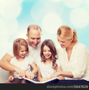 family, childhood, holidays and people - smiling mother, father and little girls reading book over blue lights background