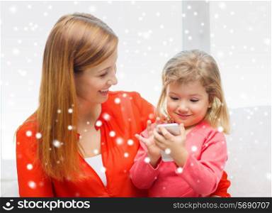 family, childhood, holidays, technology and people concept - happy mother and daughter with smartphone at home