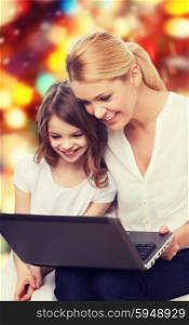 family, childhood, holidays, technology and people concept - smiling mother and little girl with laptop computer over red lights background