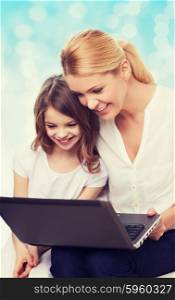 family, childhood, holidays, technology and people concept - smiling mother and little girl with laptop computer over blue lights background