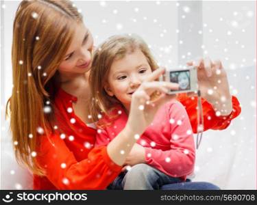 family, childhood, holidays, technology and people concept - smiling mother taking picture of daughter with digital camera at home