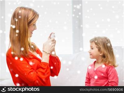 family, childhood, holidays, technology and people concept - smiling mother taking picture of daughter with digital camera at home