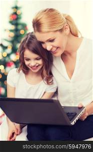 family, childhood, holidays, technology and people - smiling mother and little girl with laptop computer over living room and christmas tree background