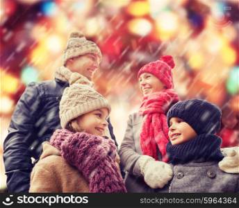 family, childhood, season, holidays and people concept - happy family in winter clothes over red lights and snow background