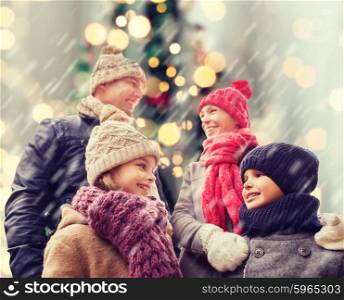 family, childhood, season, holidays and people concept - happy family in winter clothes over christmas tree lights background