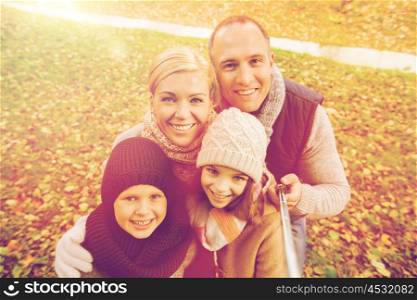 family, childhood, season, technology and people concept - happy family photographing with selfie stick in autumn park