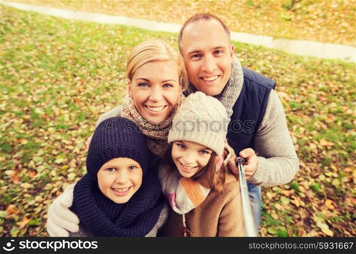 family, childhood, season, technology and people concept - happy family photographing with selfie stick in autumn park