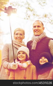 family, childhood, season, technology and people concept - happy family taking selfie with smartphone and monopod in autumn park