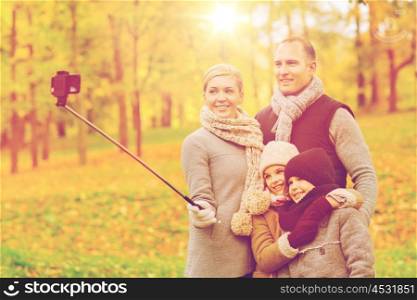family, childhood, season, technology and people concept - happy family taking selfie with smartphone and monopod in autumn park
