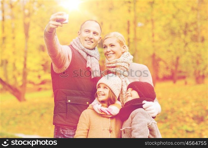 family, childhood, season, technology and people concept - happy family taking selfie with camera in autumn park