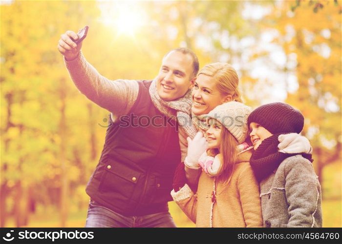 family, childhood, season, technology and people concept - happy family taking selfie with smartphone in autumn park