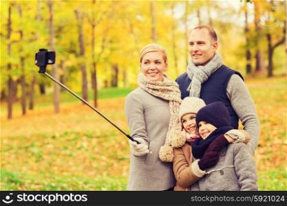family, childhood, season, technology and people concept - happy family taking selfie with smartphone and monopod in autumn park