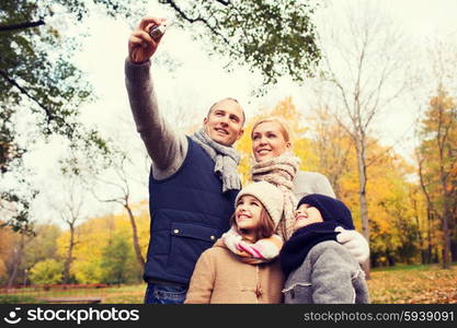 family, childhood, season, technology and people concept - happy family taking selfie with camera in autumn park