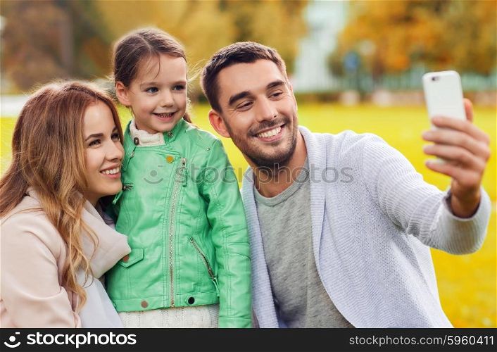 family, childhood, season, technology and people concept - happy family taking selfie by smartphone in autumn park
