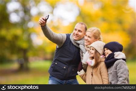 family, childhood, season, technology and people concept - happy family taking selfie with smartphone in autumn park. happy family with camera in autumn park