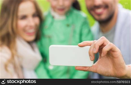family, childhood, technology and people concept - close up of happy father, mother and little daughter taking selfie by smartphone in park