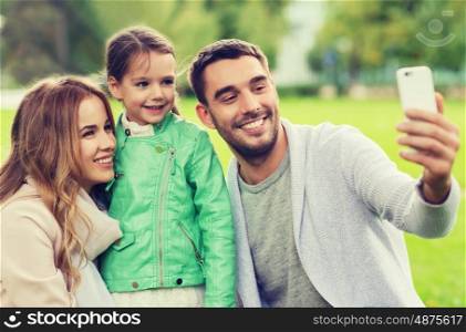 family, childhood, technology and people concept - happy family taking selfie by smartphone in park