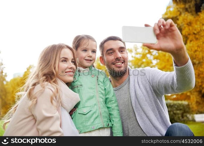 family, childhood, technology and people concept - happy father, mother and little daughter taking selfie by smartphone in autumn park
