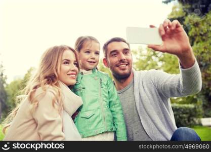 family, childhood, technology and people concept - happy father, mother and little daughter taking selfie by smartphone in park. happy family taking selfie by smartphone outdoors