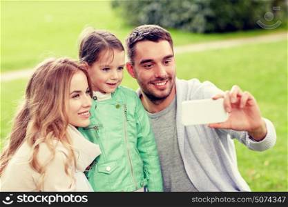 family, childhood, technology and people concept - happy father, mother and little daughter taking selfie by smartphone in park. happy family taking selfie by smartphone outdoors
