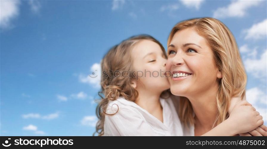 family, children and happy people concept - happy little girl hugging and kissing her mother over blue sky background