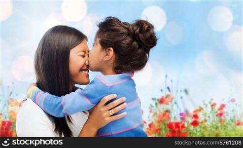 family, children and happy people concept - happy little girl hugging and kissing her mother over blue sky with lights and poppy field background