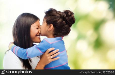family, children and happy people concept - happy little girl hugging and kissing her mother over green background