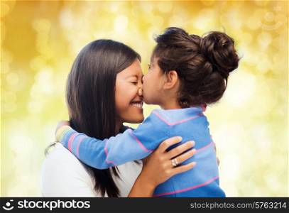 family, children and happy people concept - happy little girl hugging and kissing her mother over yellow lights background