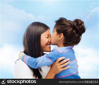 family, children and happy people concept - happy little girl hugging and kissing her mother over blue sky background