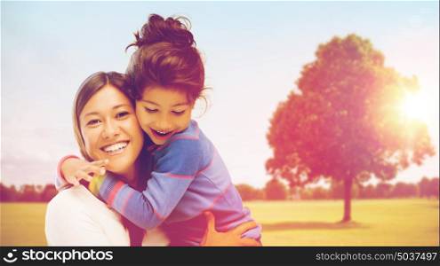 family, children and happy people concept - smiling mother and daughter hugging over oak tree at summer park background. happy mother and daughter hugging outdoors